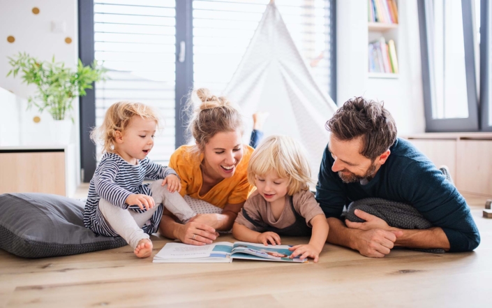 Young family with two small children indoors in bedroom reading a book._