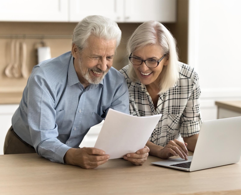Side view of a happy elderly couple looking at laptop and financial document